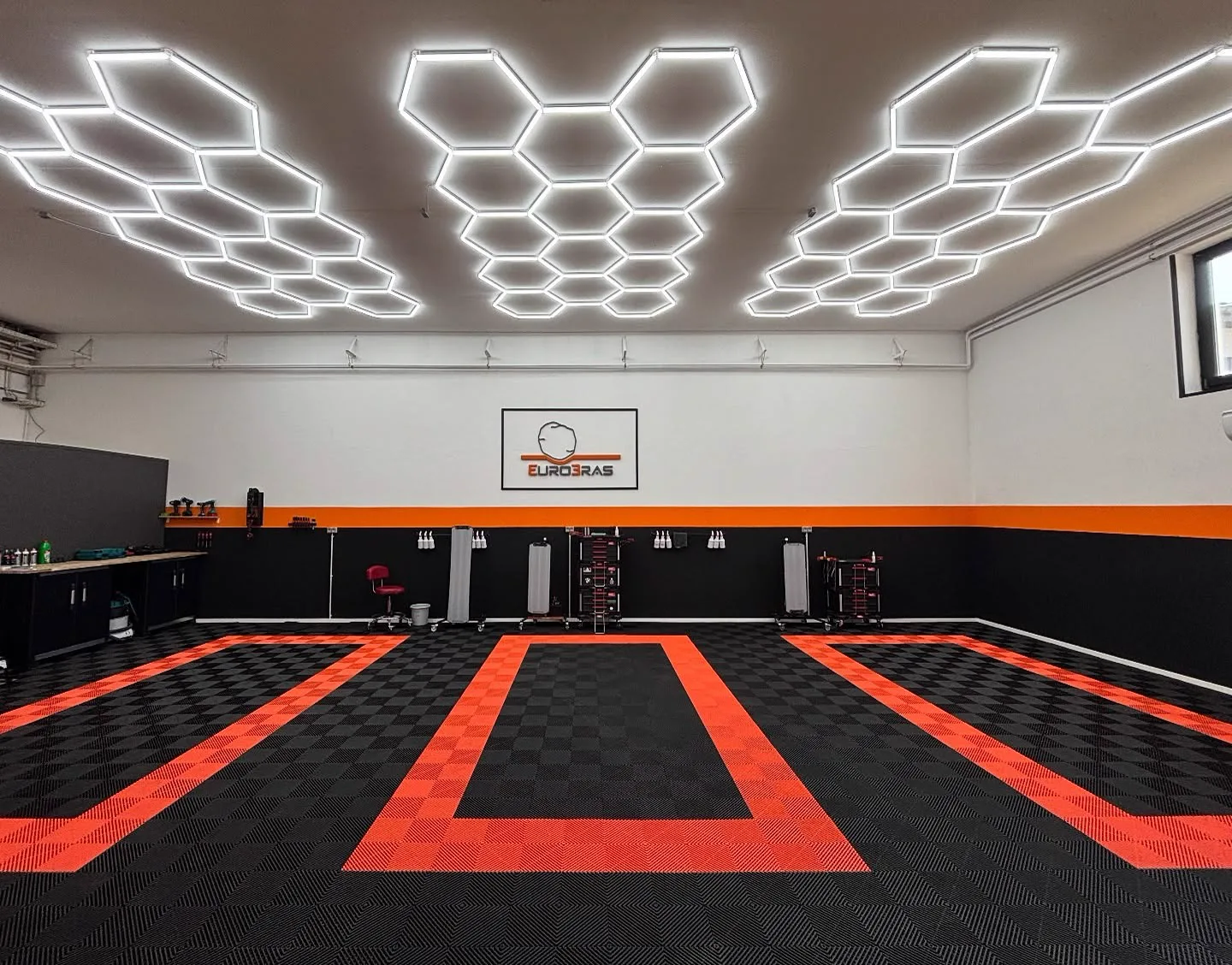 Die Werkstatt von Euro-Bras: helle Halle mit sechseckigen Leuchtpaneelen, dem Firmenlogo an der Wand und einem orange-schwarzen Boden.